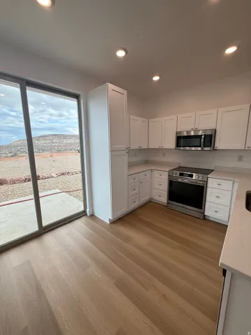 Kitchen with white cabinets, stainless steel appliances, recessed lighting, light stone countertops, and light wood-style floors