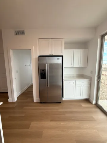 Kitchen with white cabinets, stainless steel refrigerator with ice dispenser, light countertops, and light wood-type flooring