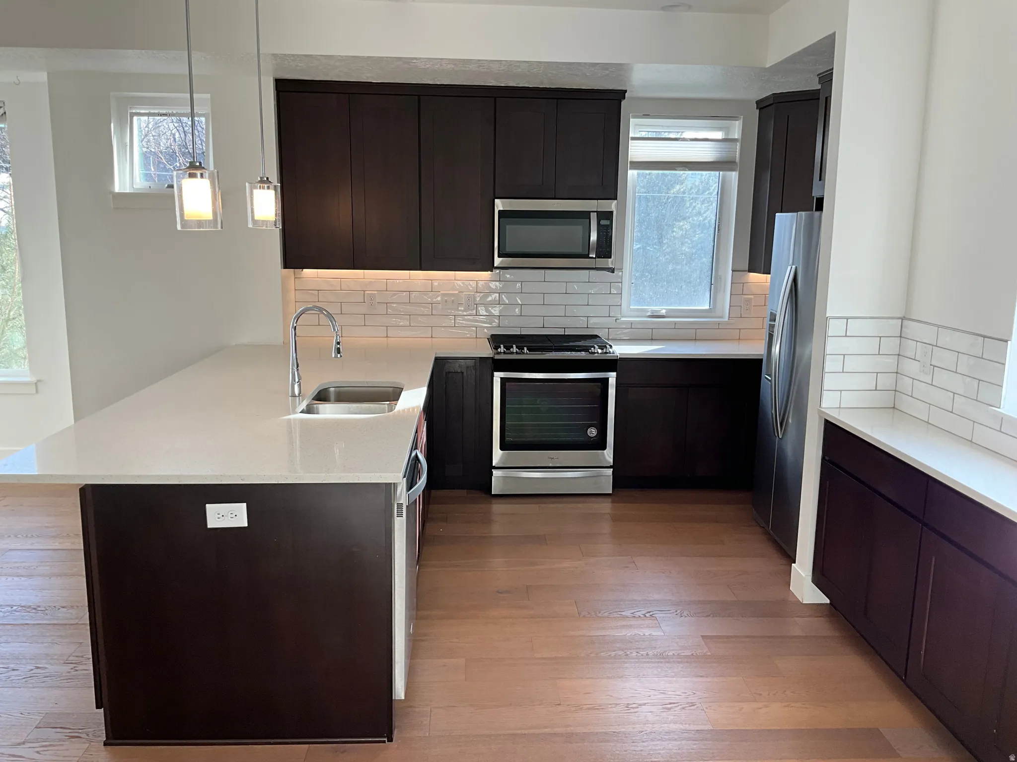 Kitchen featuring stainless steel appliances, light stone counters, backsplash, decorative light fixtures, and dark brown cabinets