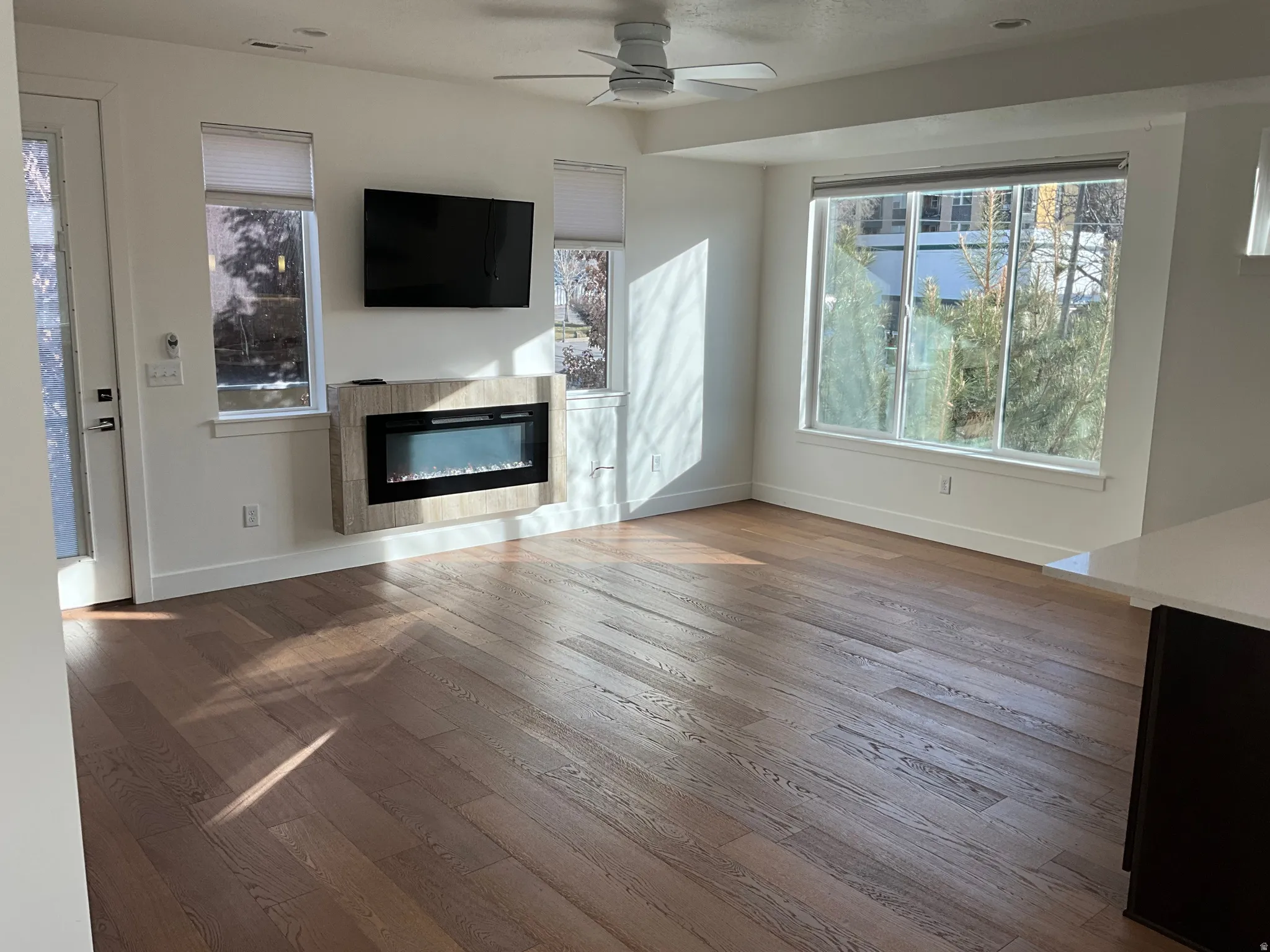 Unfurnished living room featuring a glass covered fireplace, hardwood / wood-style floors, a ceiling fan, and plenty of natural light