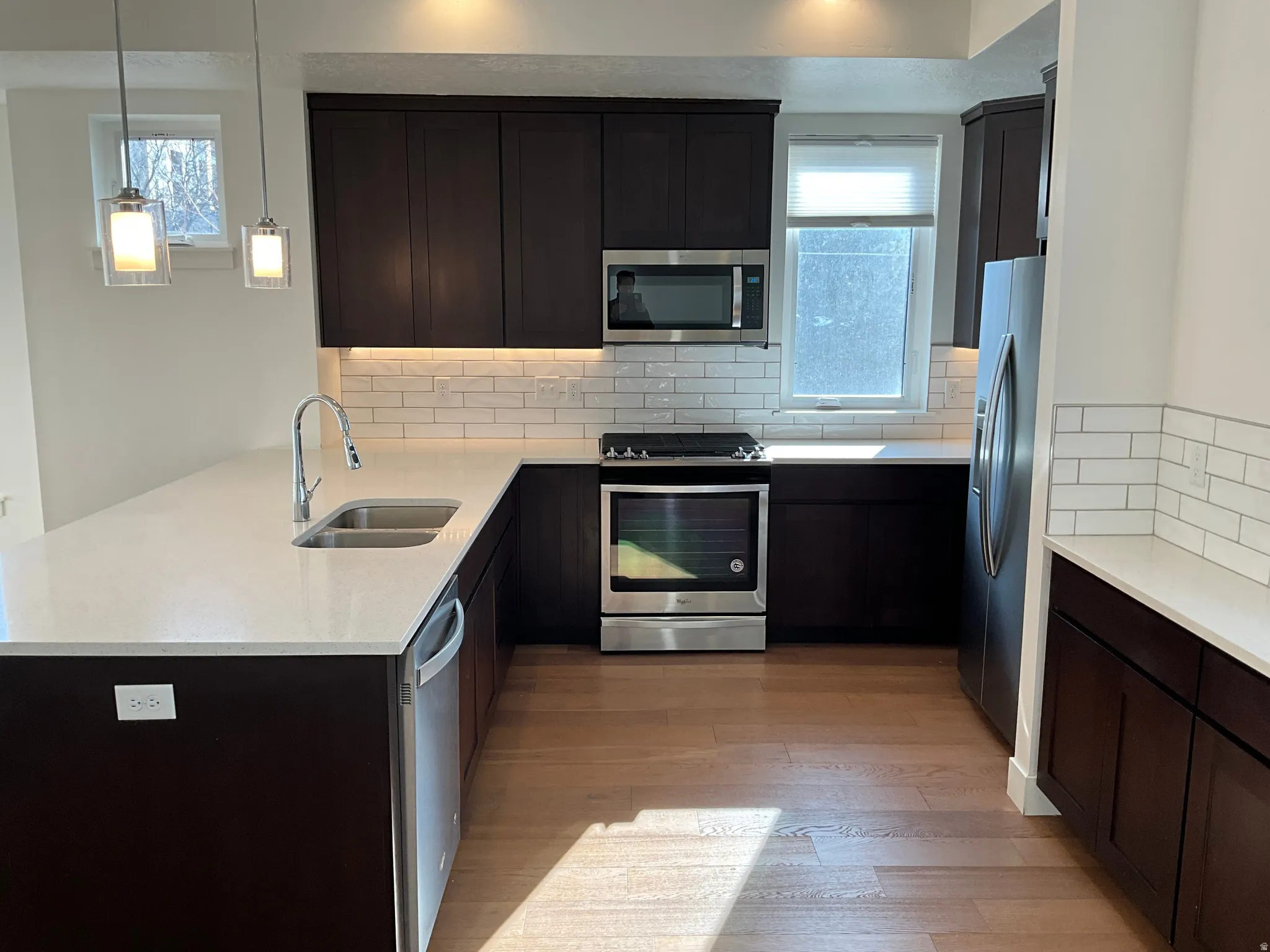 Kitchen with stainless steel appliances, light stone counters, decorative backsplash, and light wood-type flooring