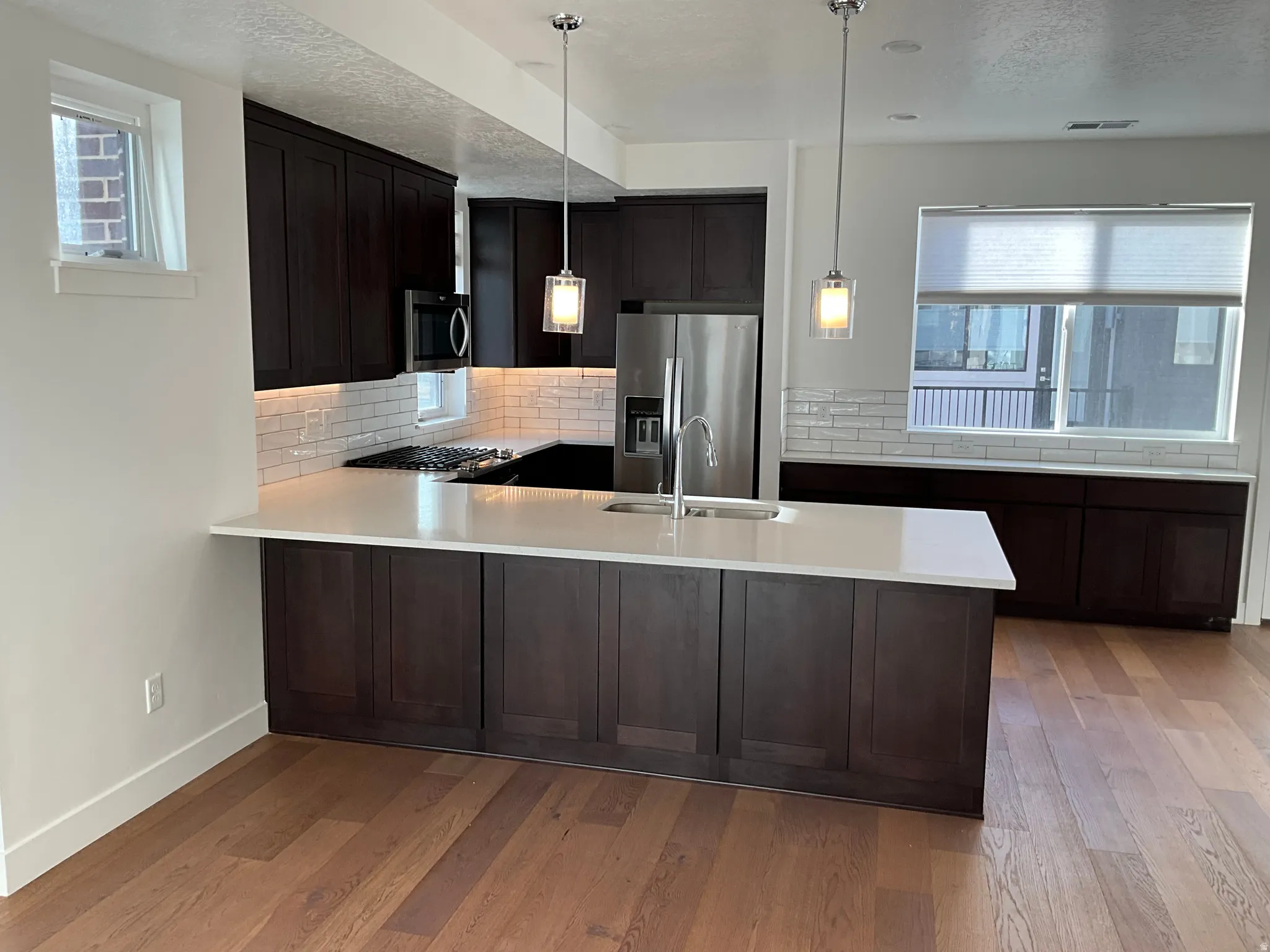 Kitchen with tasteful backsplash, a peninsula, stainless steel appliances, dark wood-type flooring, and pendant lighting