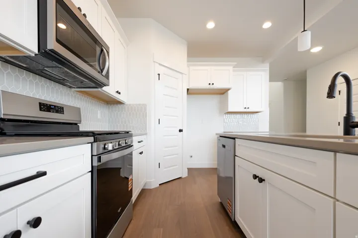 Modern kitchen featuring white cabinetry with matte black hardware, stainless steel appliances, a geometric tile backsplash, and light wood-finish flooring