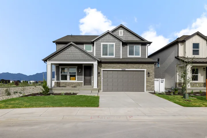 Two-story residence featuring a covered entry, stone veneer and shingle siding, an attached two-car garage, and a concrete driveway