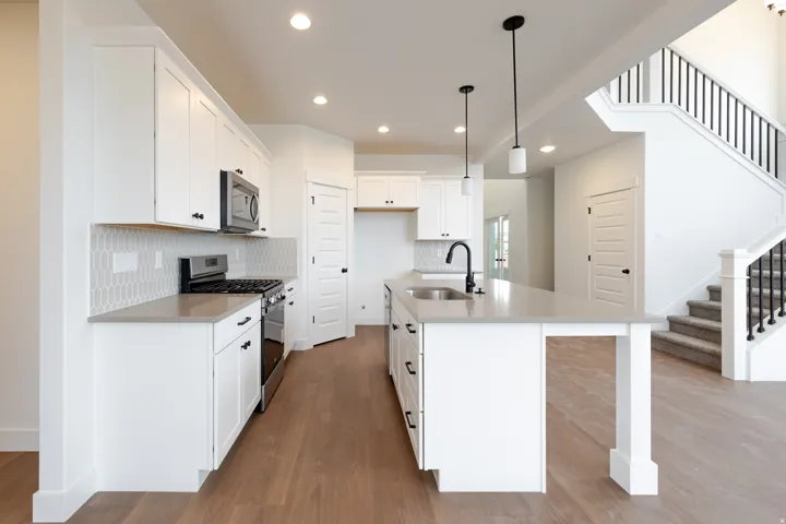 Bright kitchen featuring an island with a sink and pendant lighting, white cabinetry, stainless steel appliances, wood-finish flooring, and a decorative tile backsplash