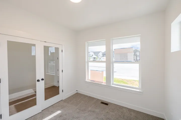 Room featuring double glass-paneled doors, two large windows, a smaller horizontal window, and neutral-toned carpet flooring