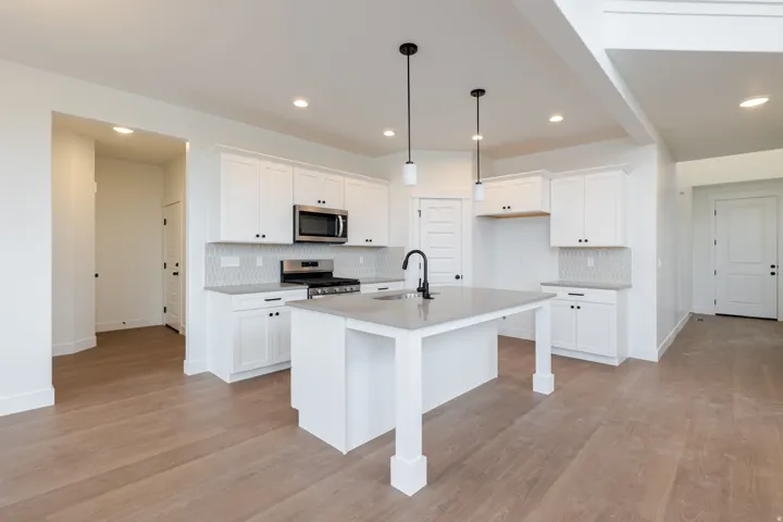 Spacious kitchen featuring an island with sink and pendant lighting, white cabinetry, integrated stainless steel appliances, and wood-finish flooring