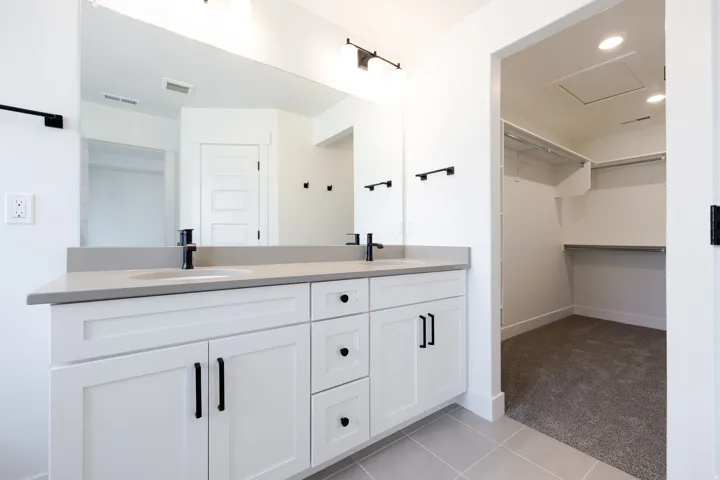 Double vanity featuring white shaker cabinetry, matte black hardware, and an expansive mirror