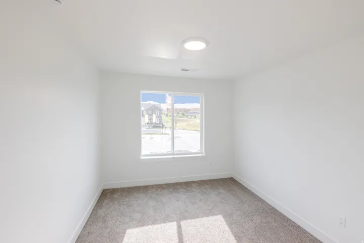Bright interior space featuring a window with exterior visibility, light grey carpeting, white baseboards, and a contemporary flush-mount ceiling light fixture
