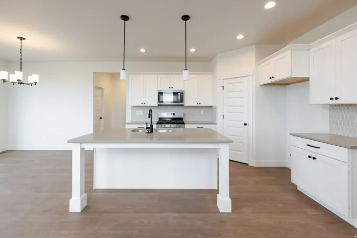 Modern kitchen featuring a central island with a sink and matte black faucet, white shaker cabinetry, stainless steel appliances, and a gray honeycomb tile backsplash