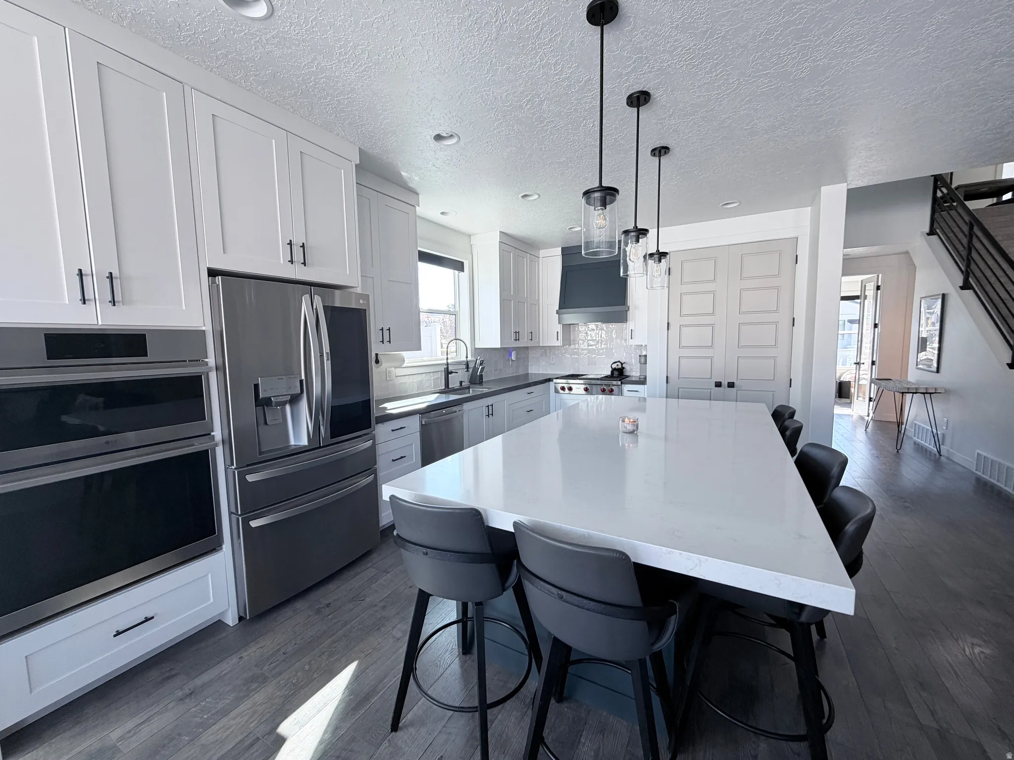 Kitchen with a kitchen bar, appliances with stainless steel finishes, a center island, decorative light fixtures, and white cabinetry