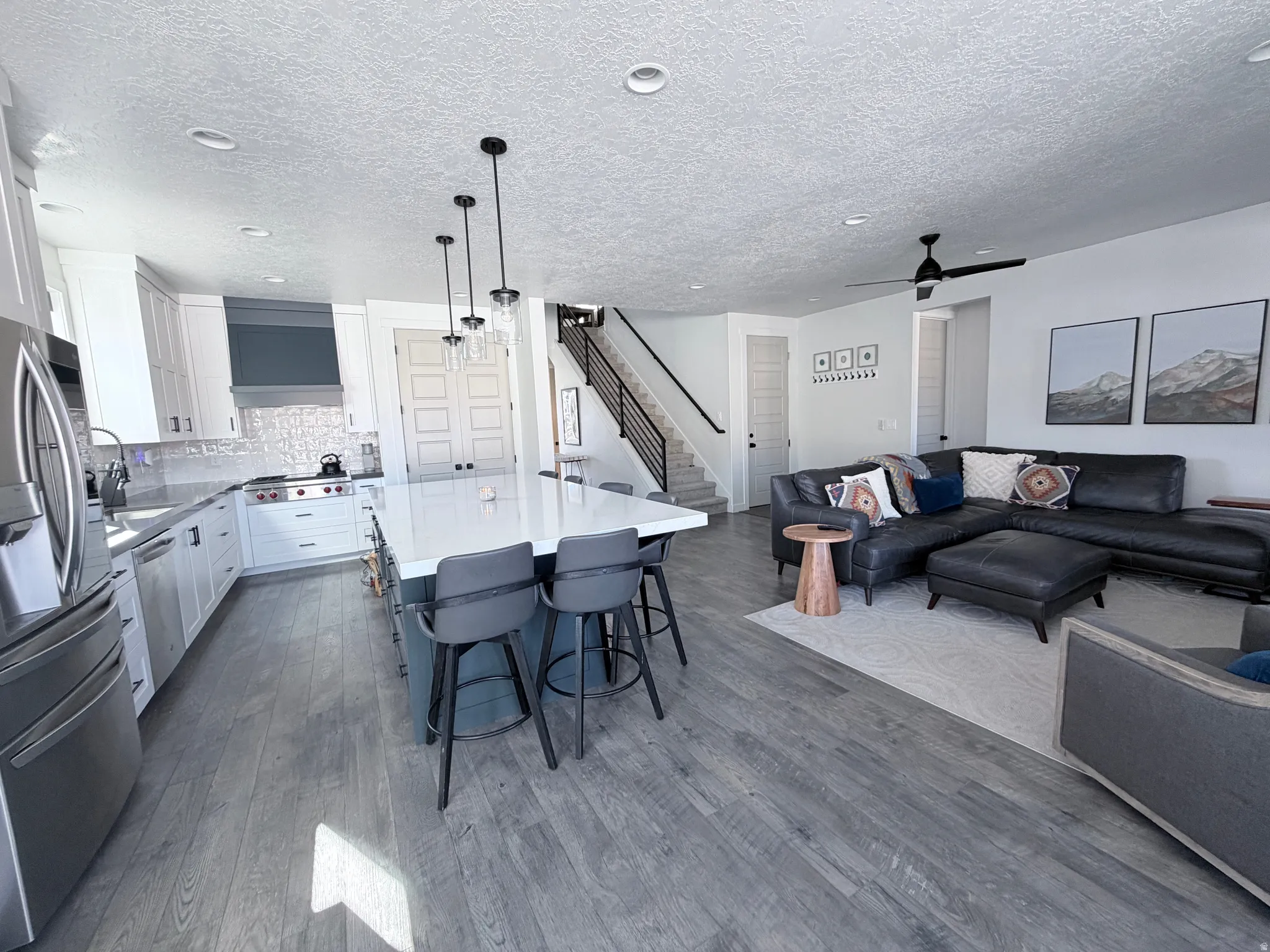 features hood, LG double oven, LG refrigerator, WOLF stovetop, cabinets to ceiling, extra large island and 6 barstools, living room with italian leather sofa and LG TV.