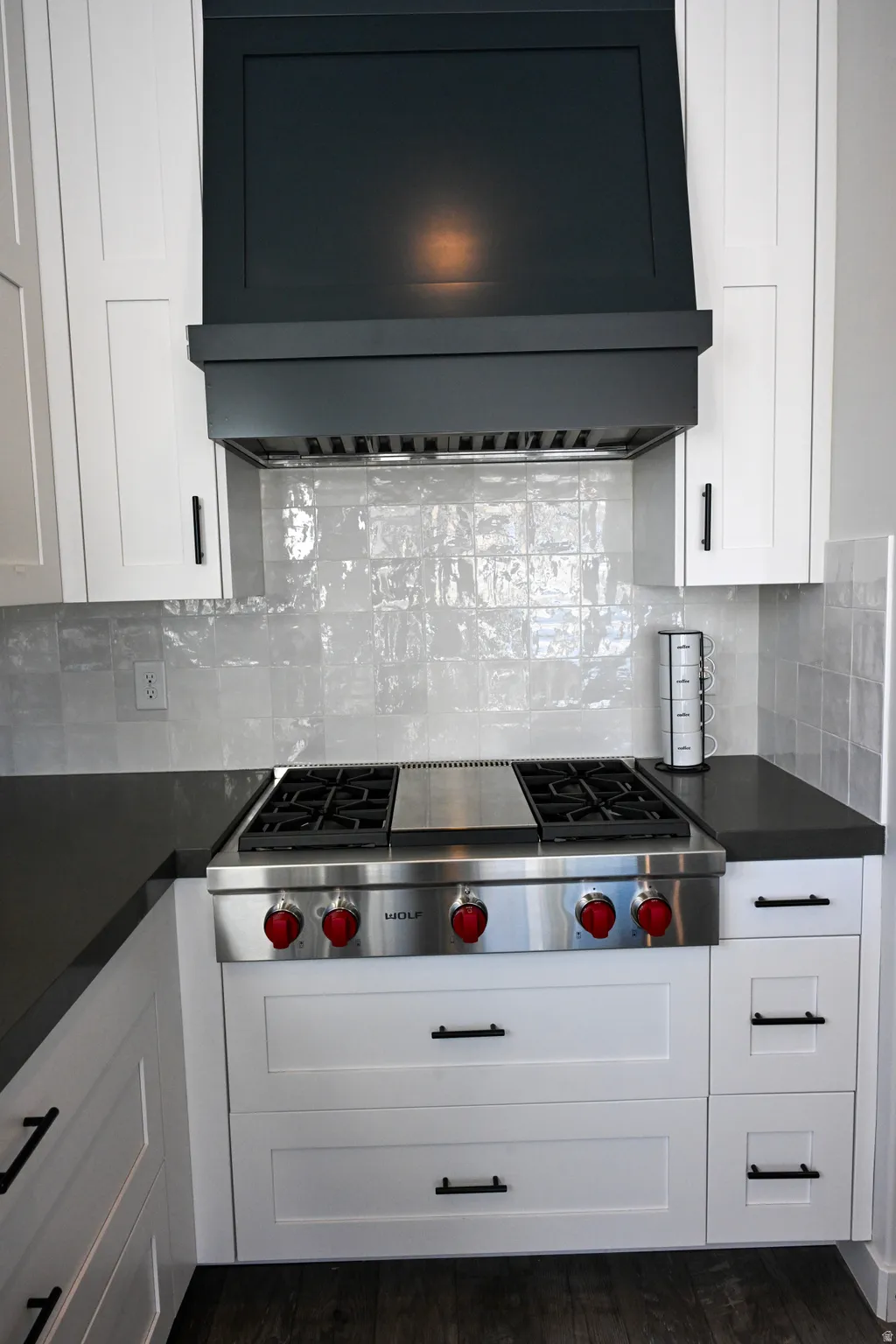 Kitchen with range hood, stainless steel gas stovetop, decorative backsplash, and white cabinetry
