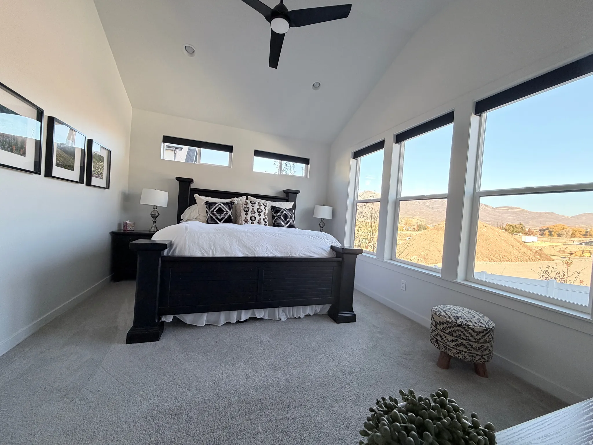 Carpeted bedroom with vaulted ceiling, a mountain view, and ceiling fan, Lutron electronic shades and king bedroom furniture, bedding and decor