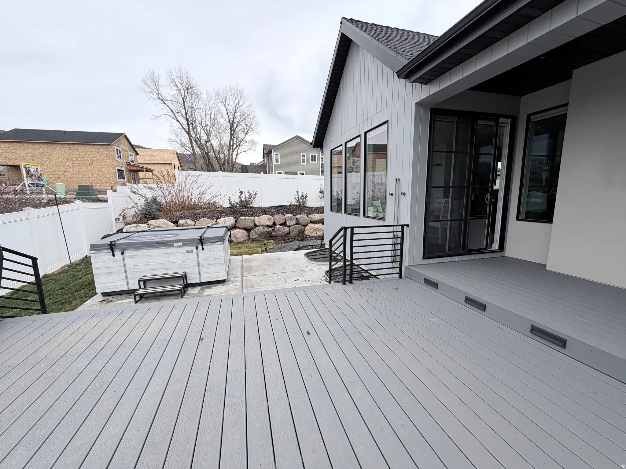 Extra large patio featuring a hot tub and landscaped fenced backyard that includes berry bushes and a rose garden following the east side of the home.