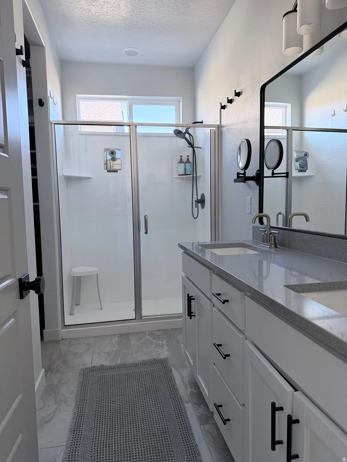 Full bathroom with double vanity, a stall shower, a textured ceiling, and light finish flooring