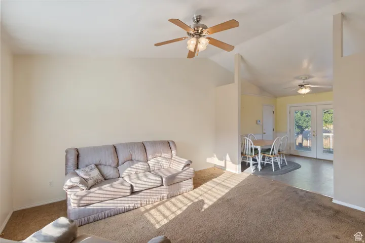 Carpeted living room featuring lofted ceiling, ceiling fan, and french doors