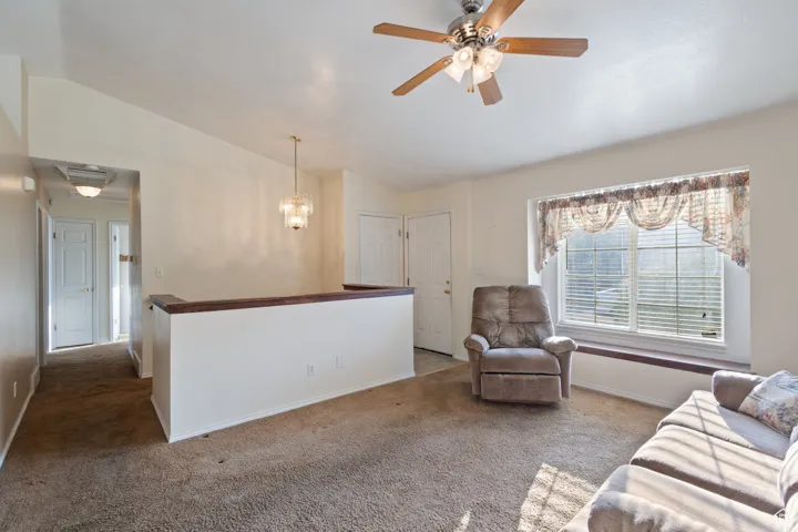 Carpeted living area featuring lofted ceiling, suspended lighting, and a ceiling fan