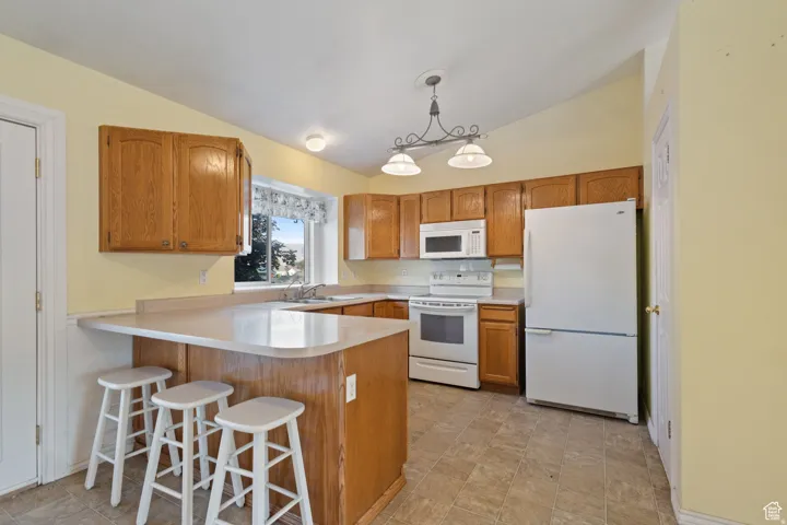 Kitchen with a breakfast bar area, vaulted ceiling, white appliances, light countertops, and hanging light fixtures