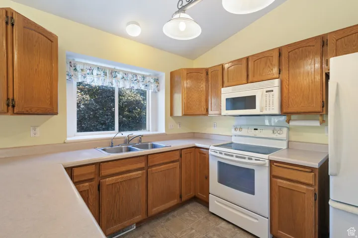 Kitchen with white appliances, vaulted ceiling, light countertops, wood finish cabinets, and decorative light fixtures
