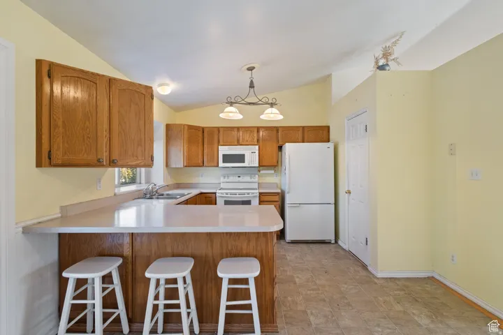 Kitchen with a peninsula, a kitchen bar, light countertops, white appliances, and hanging light fixtures