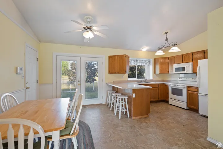 Kitchen with light countertops, white appliances, a kitchen breakfast bar, hanging light fixtures, and french doors