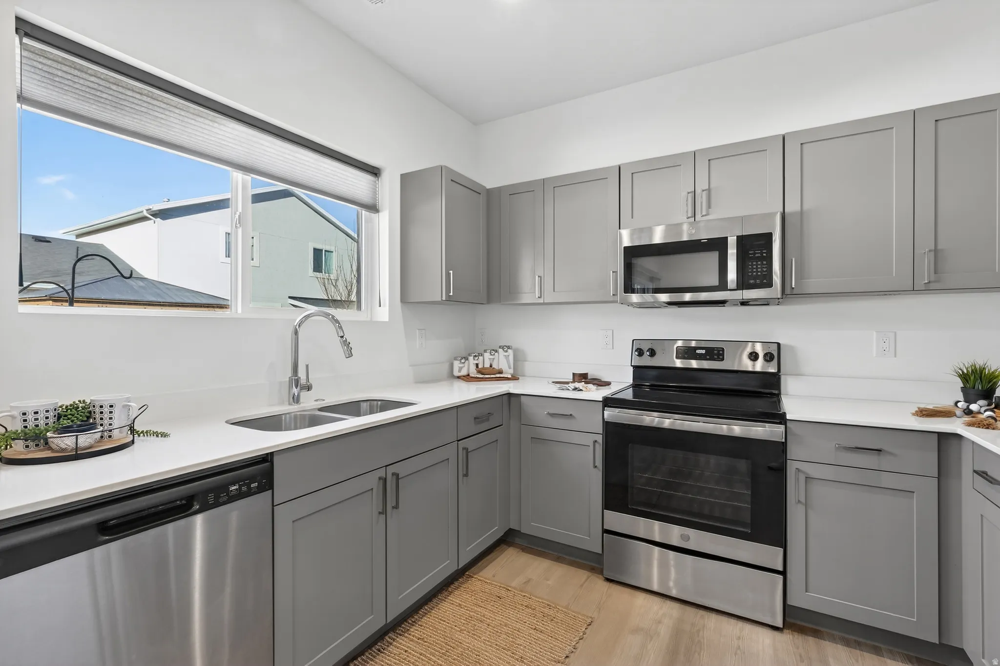 Kitchen with gray cabinetry, stainless steel appliances, light wood-style flooring, and light stone counters