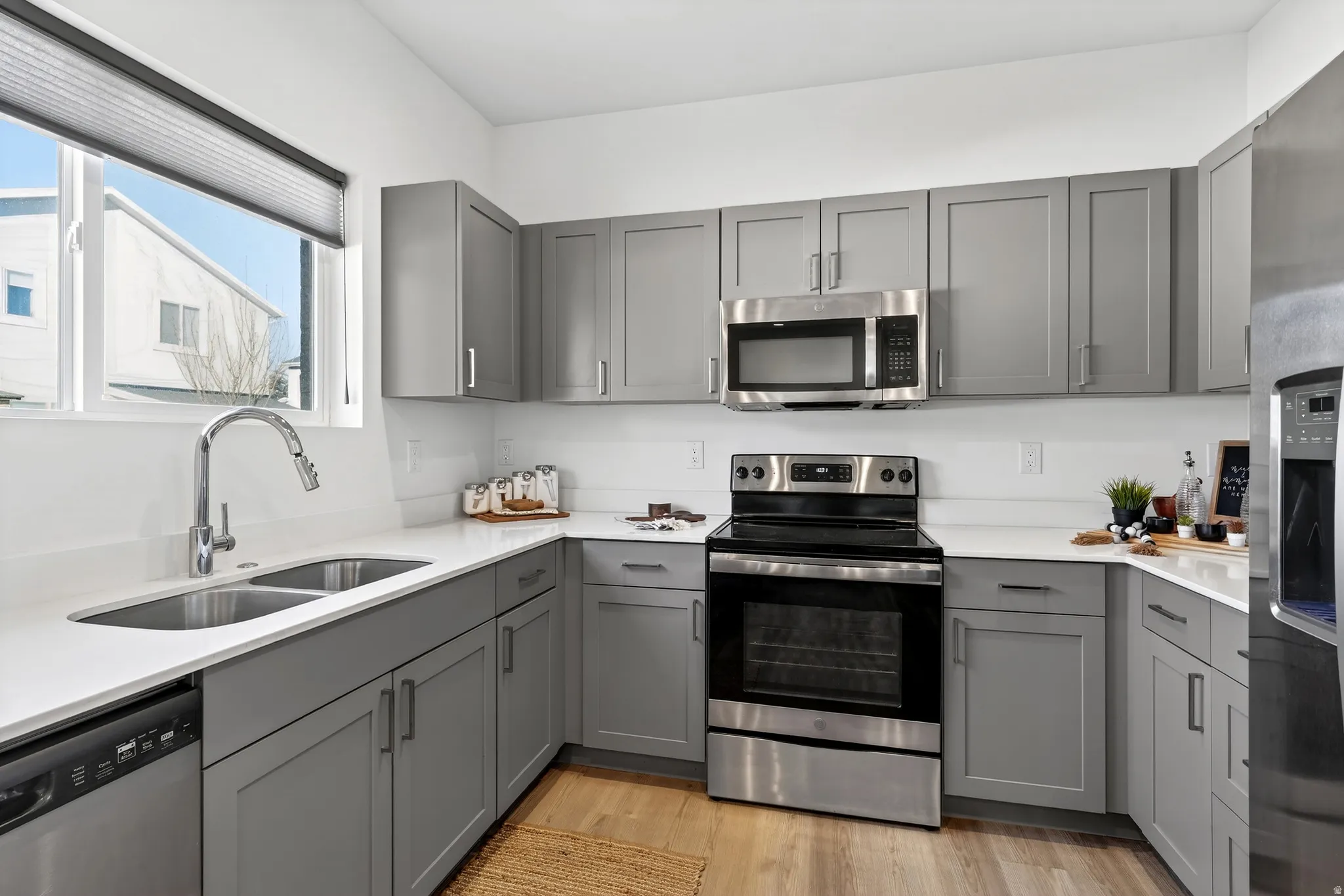Kitchen featuring gray cabinetry, appliances with stainless steel finishes, light wood-type flooring, and light stone countertops