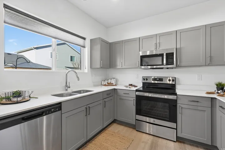 Kitchen with gray cabinetry, stainless steel appliances, light wood-style flooring, and light stone counters