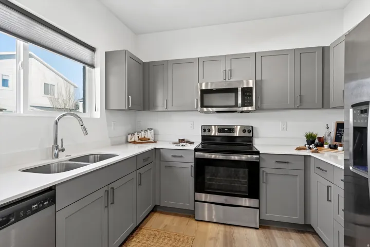 Kitchen featuring gray cabinetry, appliances with stainless steel finishes, light wood-type flooring, and light stone countertops