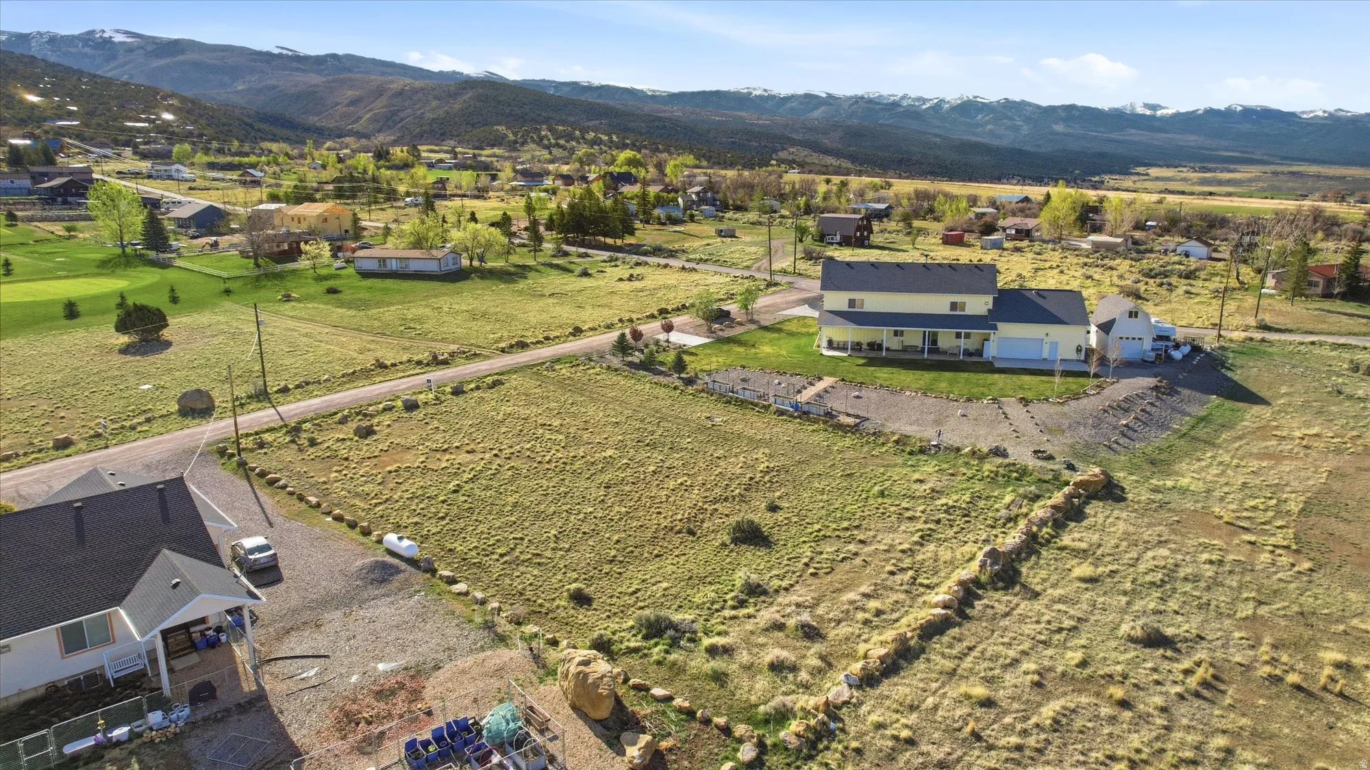 Spacious property featuring a two-story residence with a multi-car garage, expansive grounds, a gravel driveway, and distant mountain backdrops
