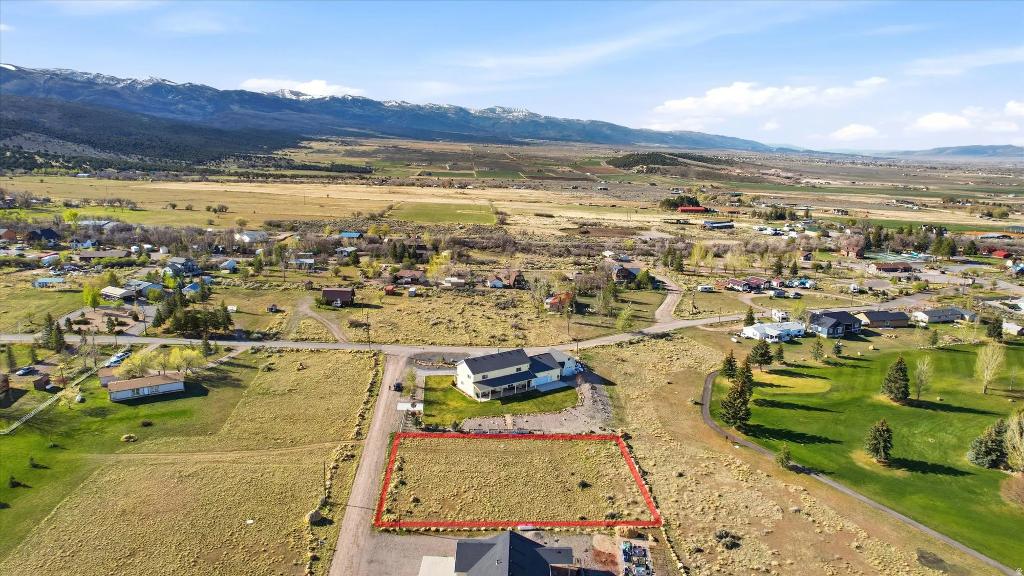 Expansive land parcel featuring a grass-covered lot, a gravel road, and surrounding undeveloped terrain
