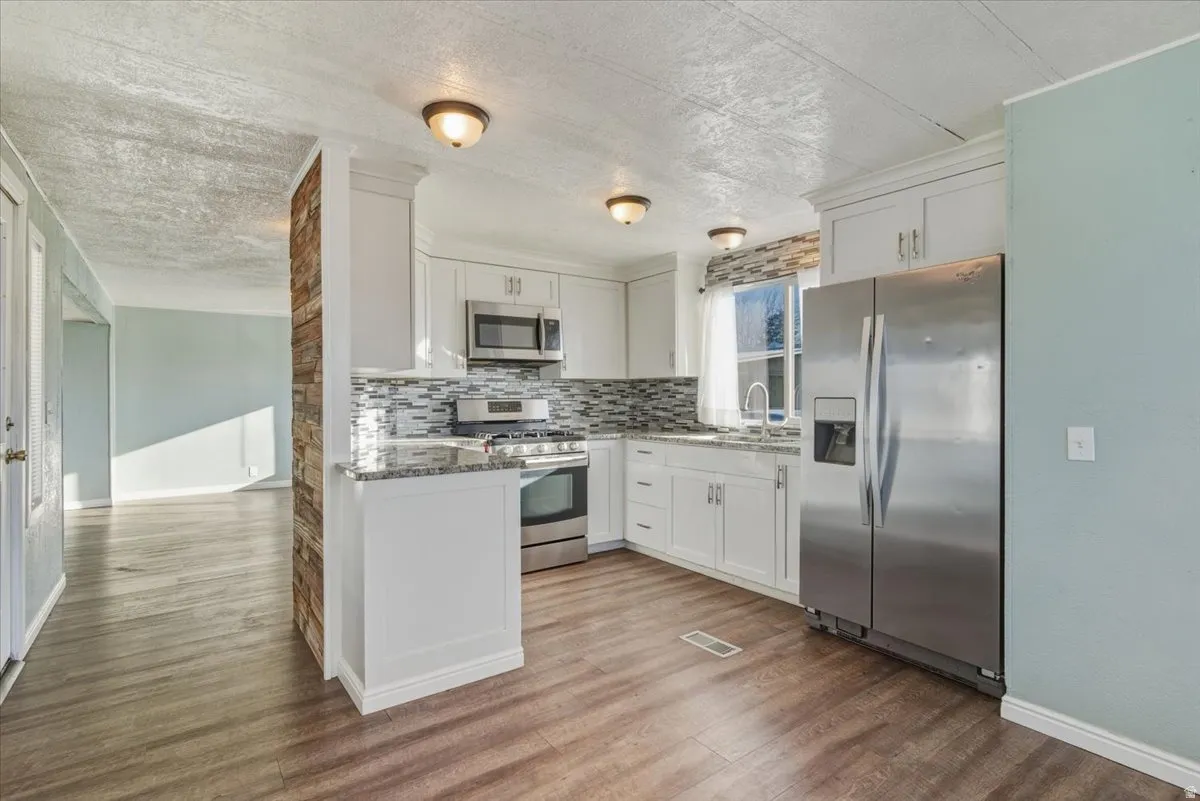 Kitchen with  stainless steel appliances, granite countertops, white cabinetry, tiled backsplash, and light wood-style flooring