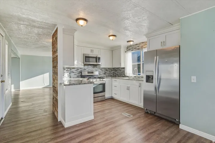 Kitchen with  stainless steel appliances, granite countertops, white cabinetry, tiled backsplash, and light wood-style flooring