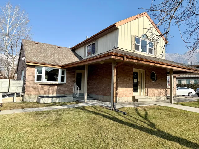 Farmhouse with a front lawn, brick siding, a shingled roof, a large porch, and board and batten siding