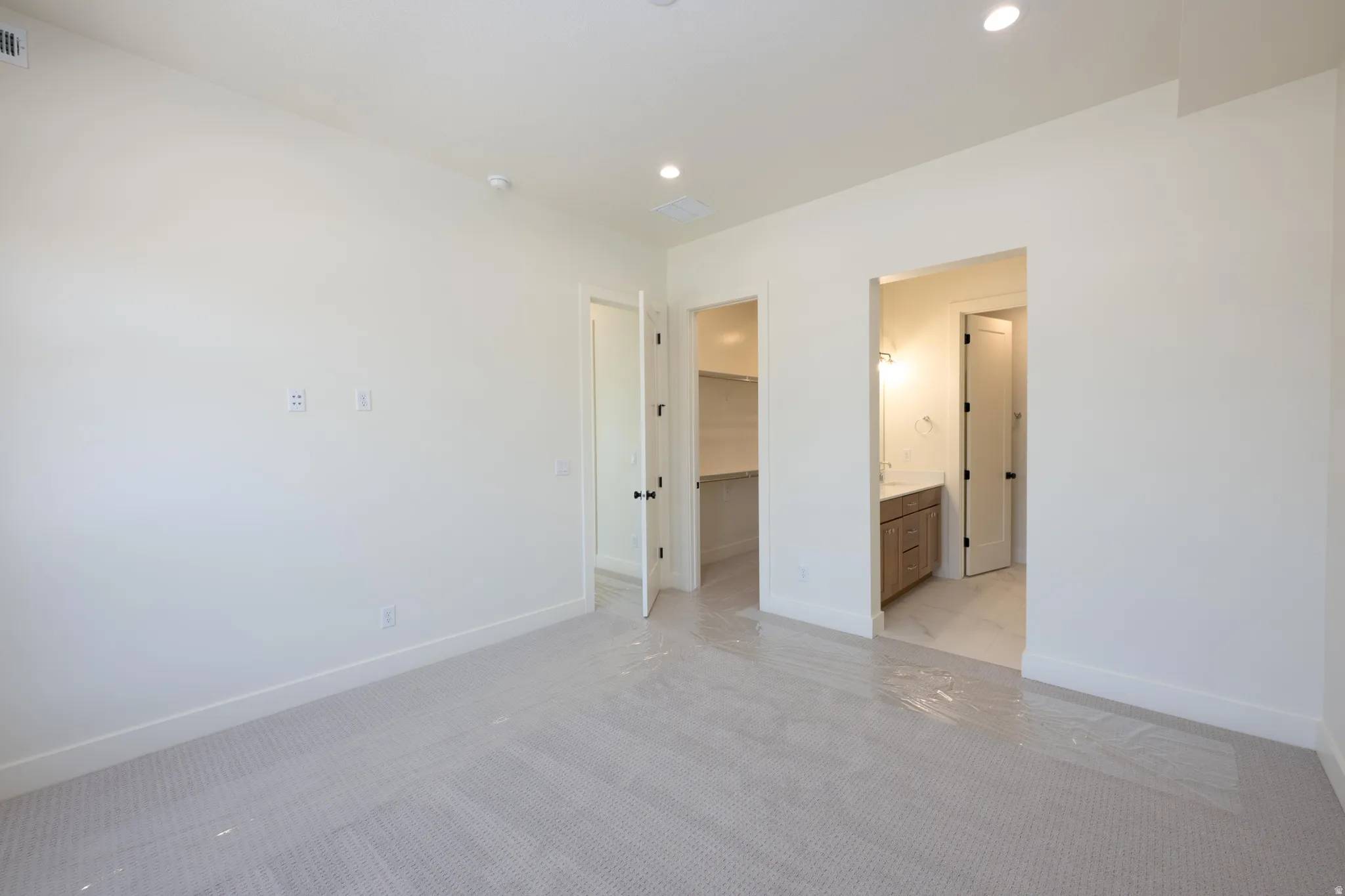 Unfurnished bedroom featuring light colored carpet, a walk in closet, recessed lighting, and connected bathroom