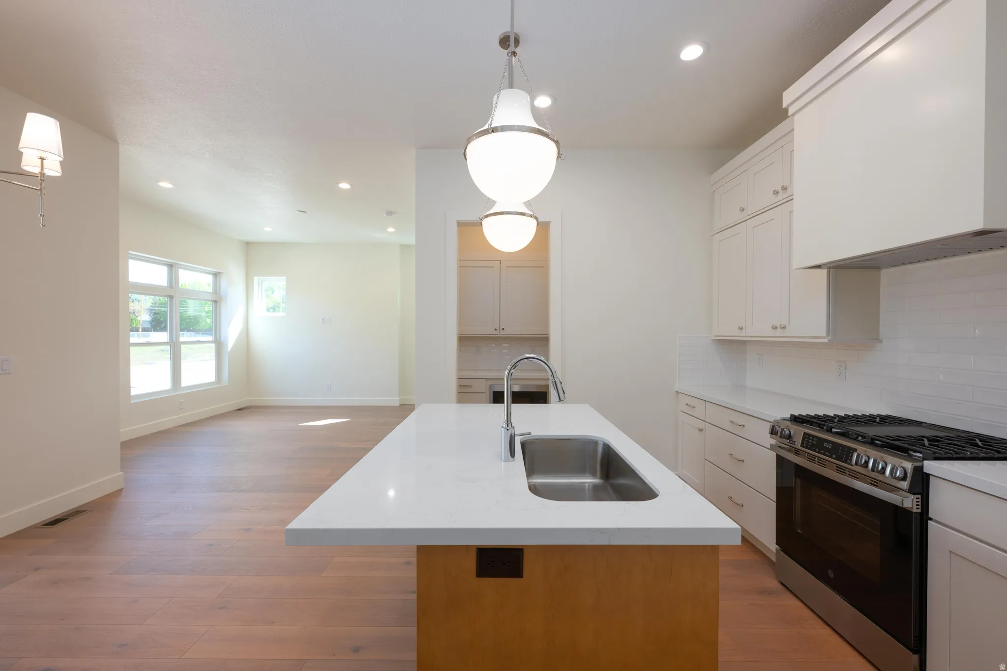 Kitchen with a center island with sink, stainless steel range with gas cooktop, backsplash, light wood-type flooring, and open floor plan