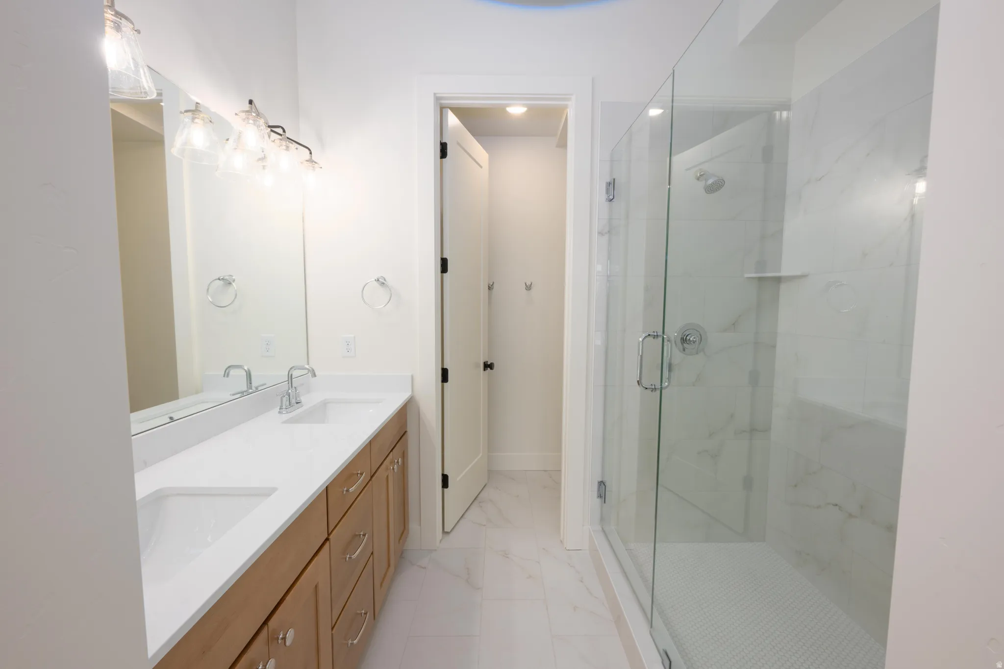 Full bathroom featuring double vanity, a marble finish shower, and light marble finish flooring