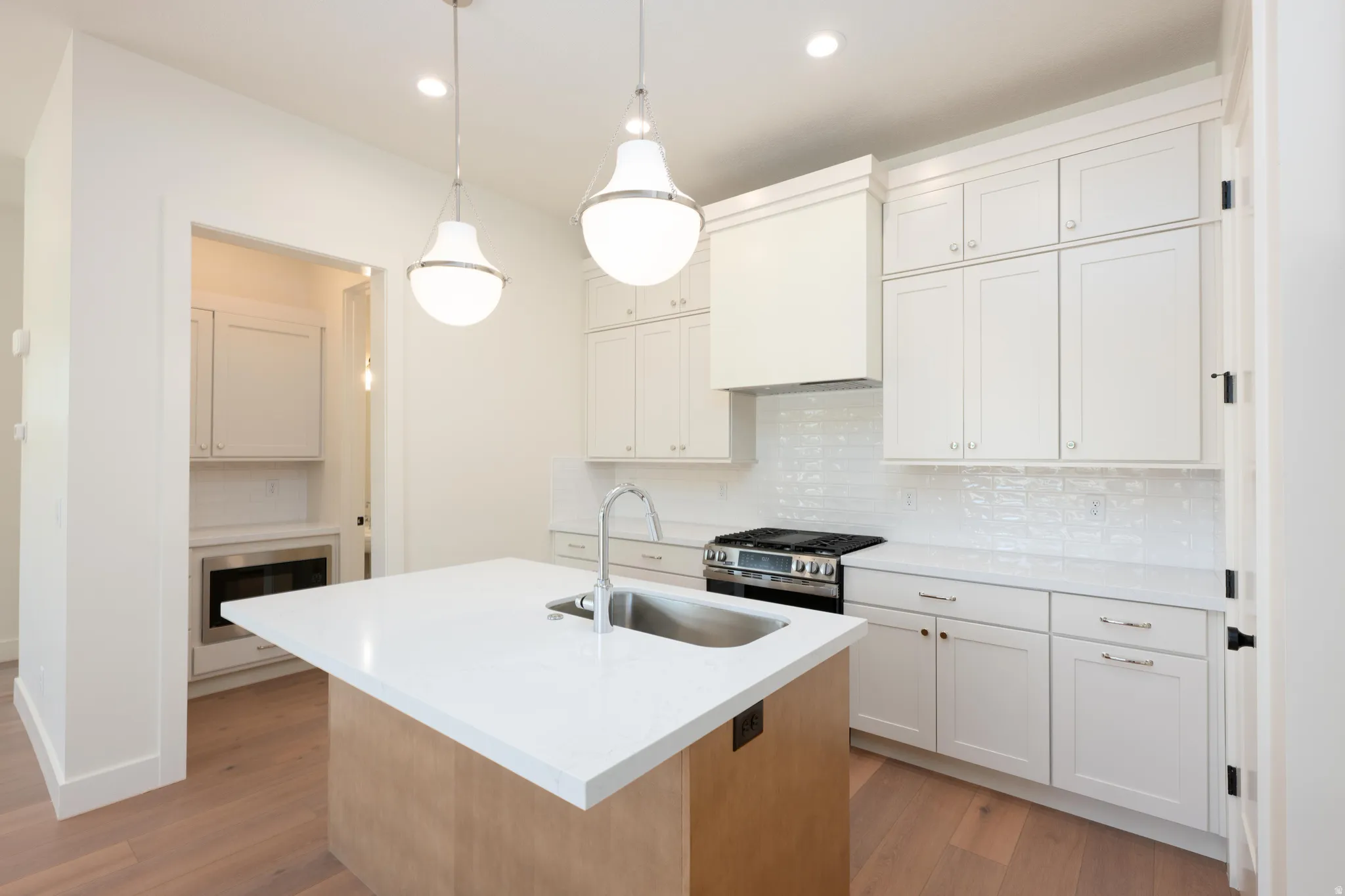 Kitchen featuring an island with sink, stainless steel appliances, backsplash, light wood finished floors, and dual tone cabinets