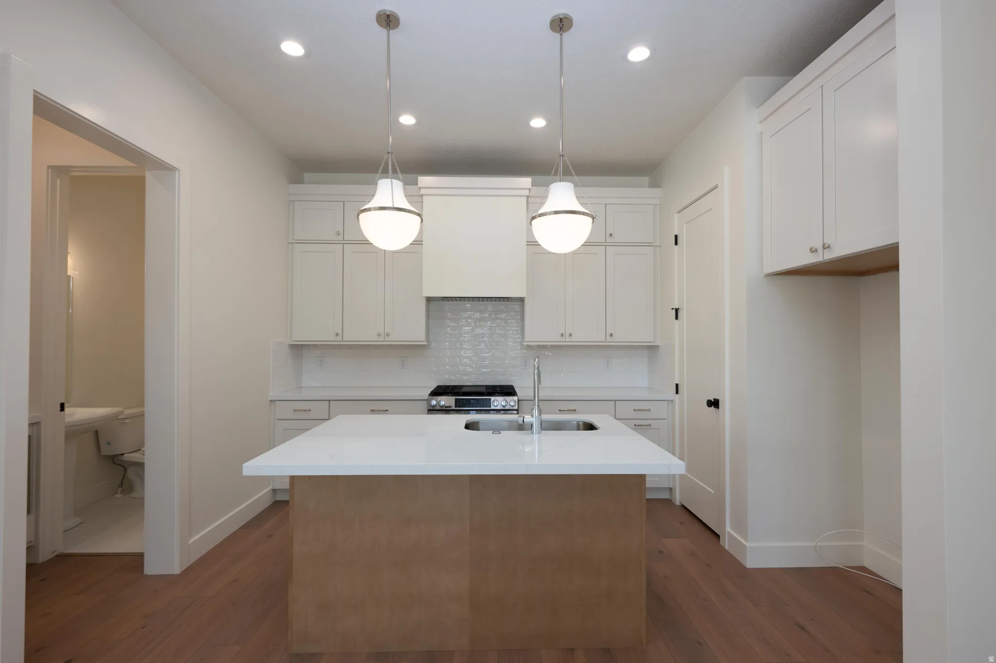 Kitchen with a center island with sink, hanging light fixtures, gas range, light stone countertops, and dark wood-style floors