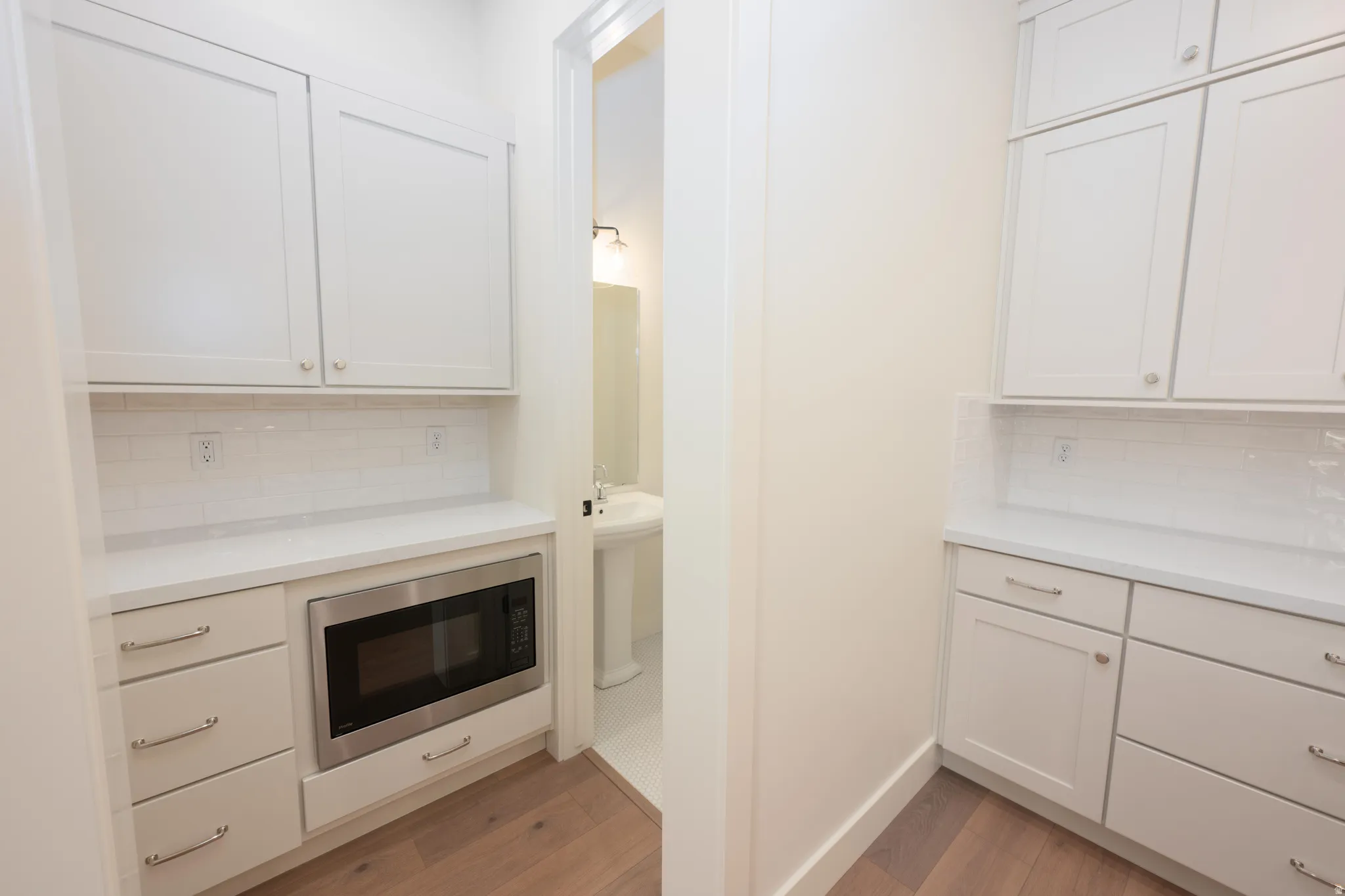 Kitchen featuring tasteful backsplash, white cabinetry, built in microwave, and light wood-type flooring