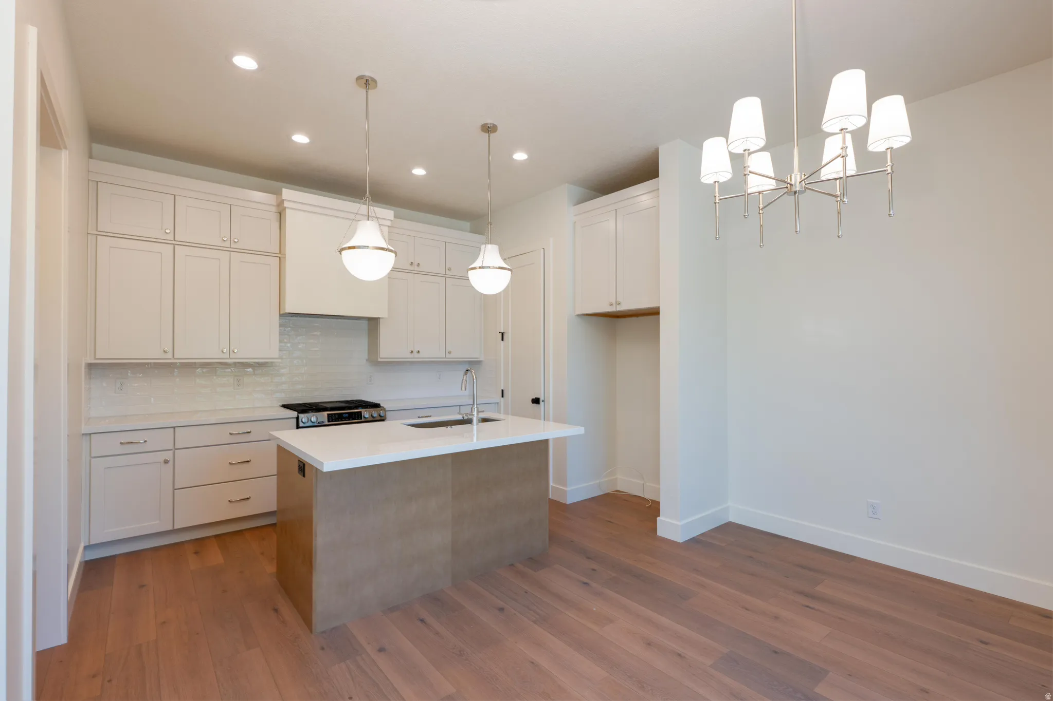 Kitchen featuring an island with sink, suspended lighting, tasteful backsplash, light wood-type flooring, and two tone cabinetry