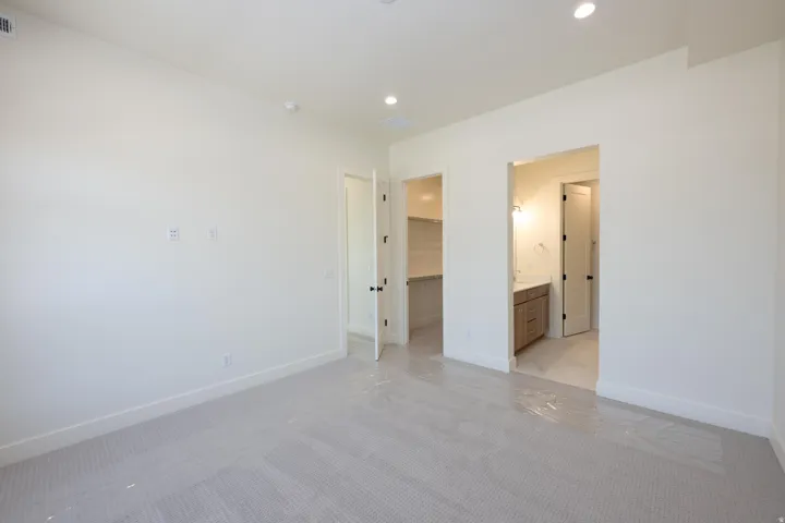 Unfurnished bedroom featuring light colored carpet, a walk in closet, recessed lighting, and connected bathroom