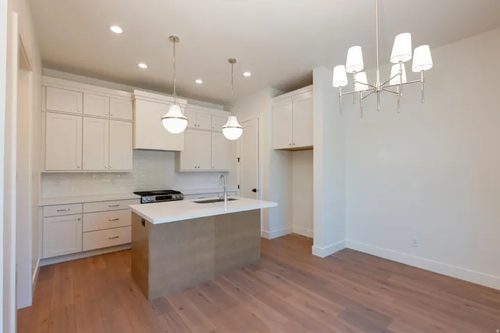 Kitchen featuring an island with sink, suspended lighting, tasteful backsplash, light wood-type flooring, and two tone cabinetry