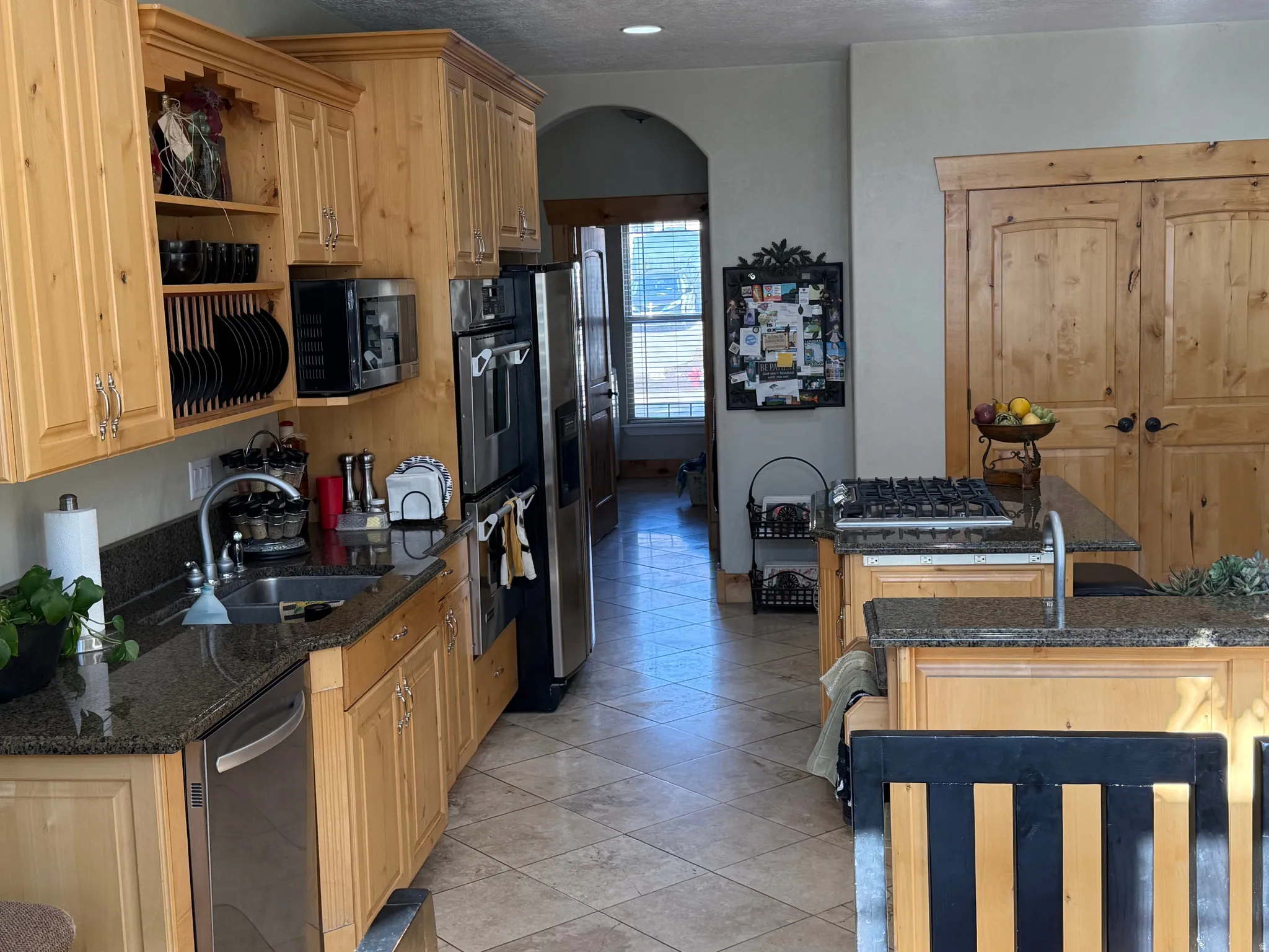 Kitchen with open shelves, arched walkways, stainless steel appliances, dark stone counters, and light tile patterned flooring