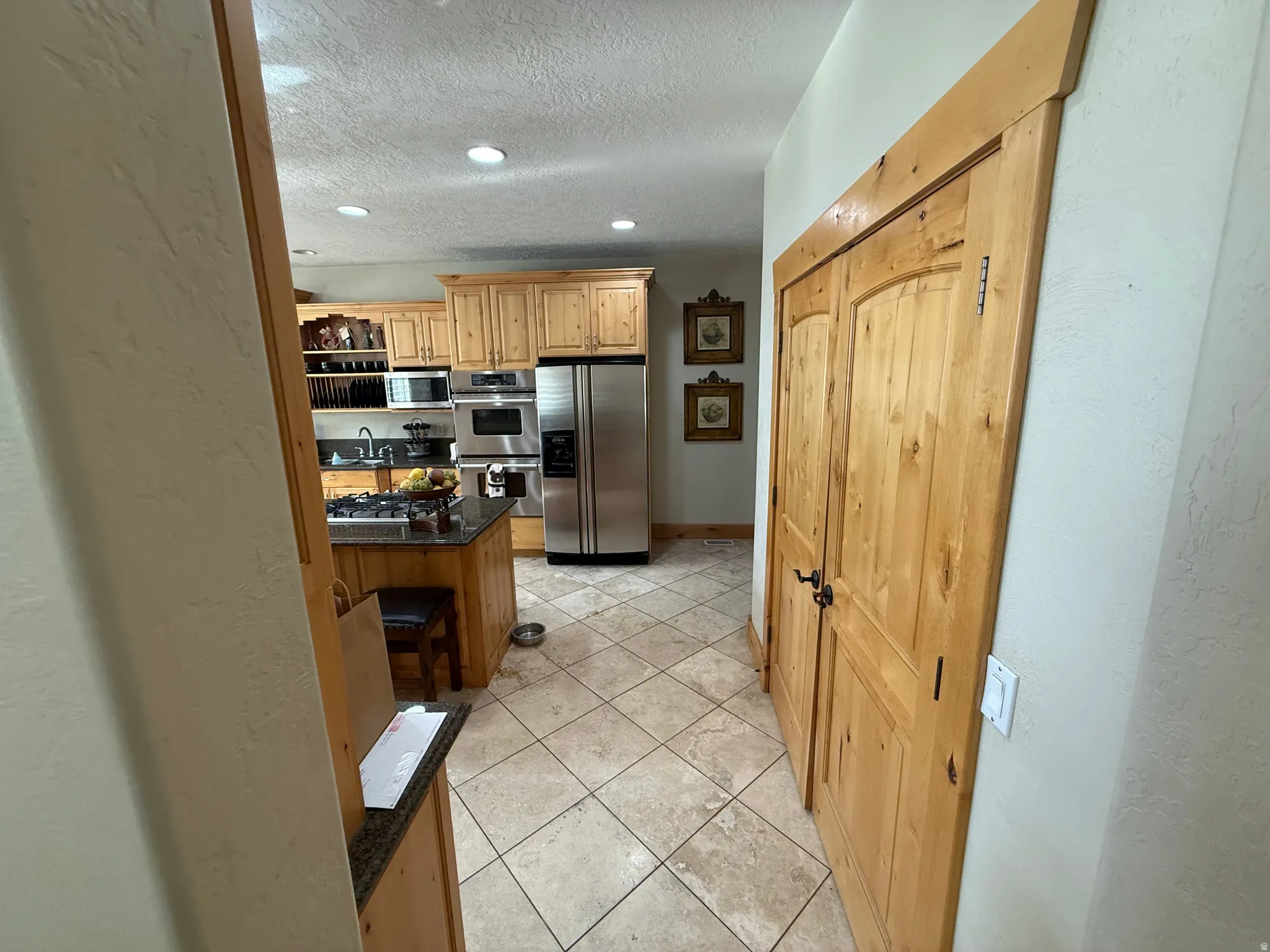 Kitchen with a textured wall, stainless steel appliances, light tile patterned floors, a textured ceiling, and dark stone countertops