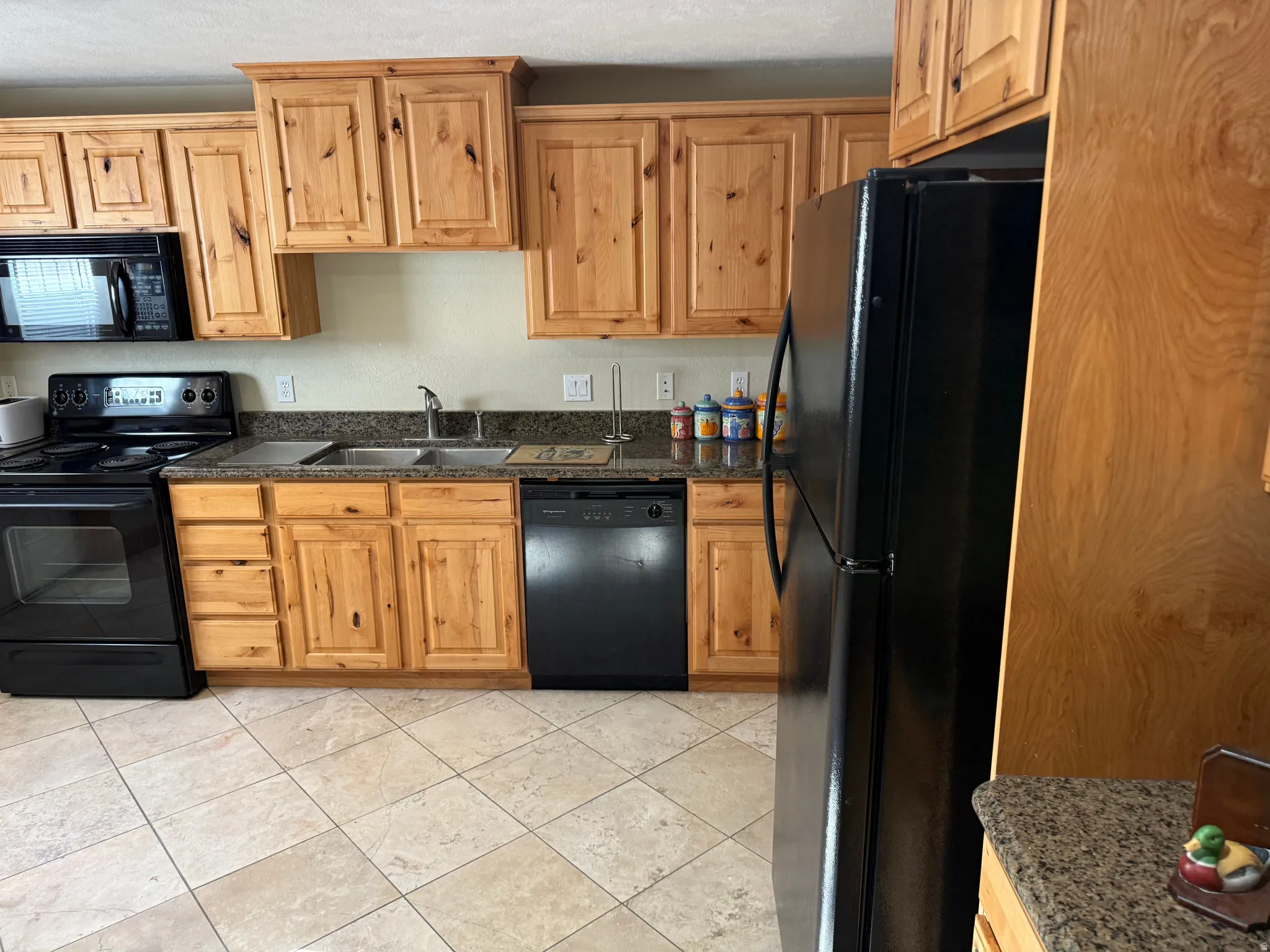 Kitchen featuring black appliances, light tile patterned floors, and dark stone countertops