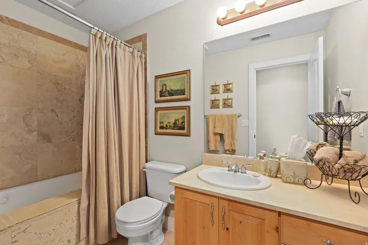 Bathroom featuring a built-in tub with tile surround, a single vanity with wood cabinetry, an oval undermount sink, and a large wall-mounted mirror
