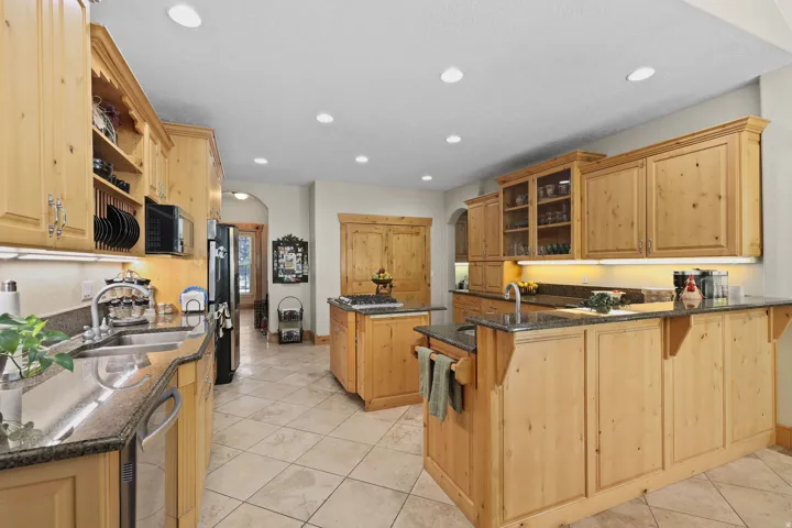 Expansive kitchen featuring natural wood cabinetry, recessed lighting, and a double-basin stainless steel sink