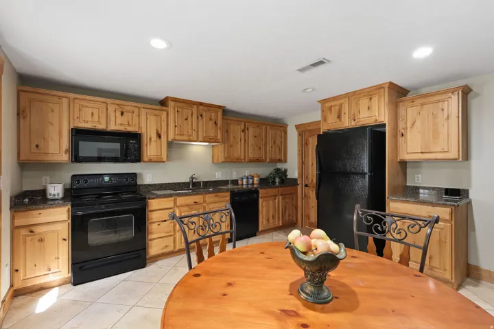 Kitchen featuring wood cabinetry, black appliances, granite-style countertops, and tile flooring